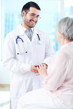 Foto eines Arztes, der die Hand einer älteren Patientin hält und ihr lächelnd zuhört.