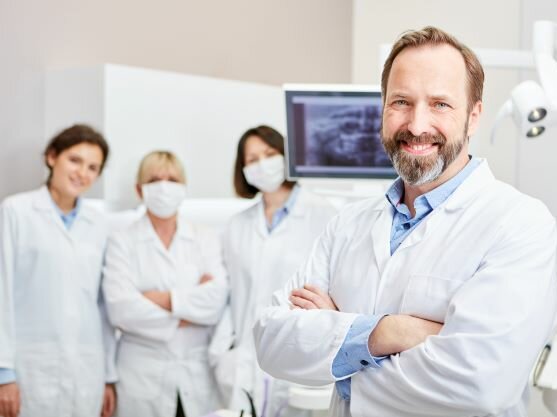 Zahnarzt mit Mitarbeiterinnen im Hintergrund