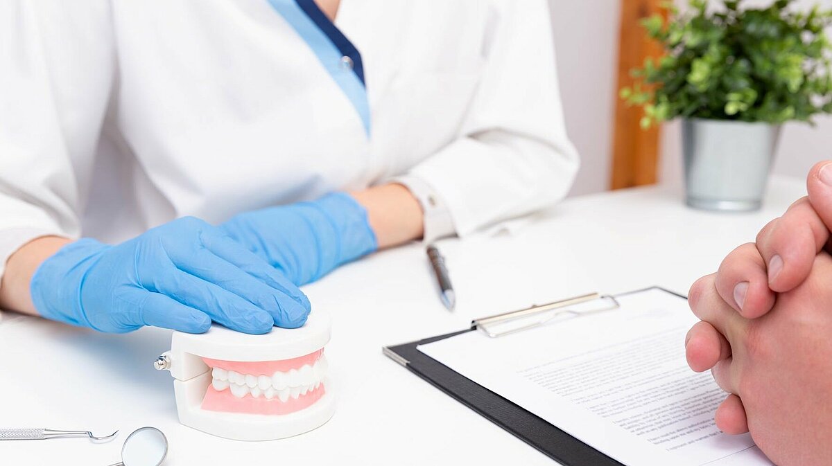 Zahnärztin und Patient sitzen sich am Schreibtisch gegenüber und sprechen