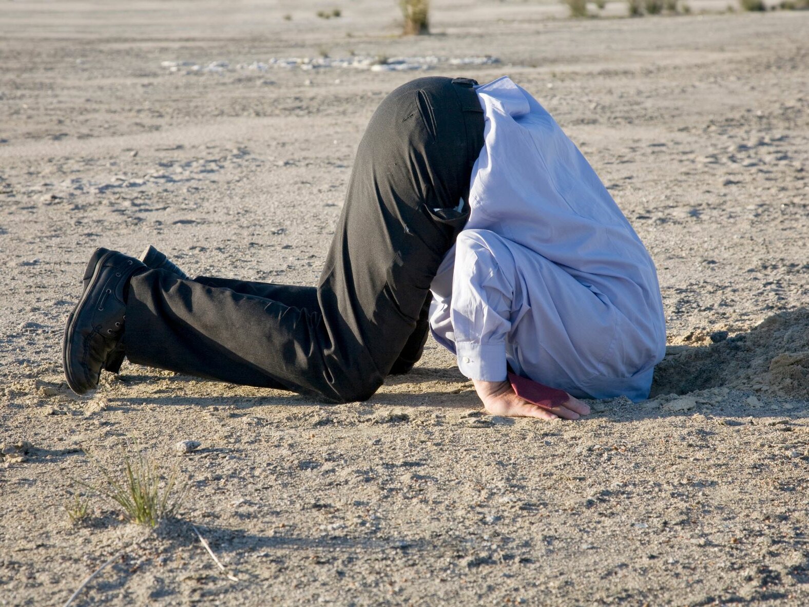 Mann im Anzug steckt den Kopf in den Sand