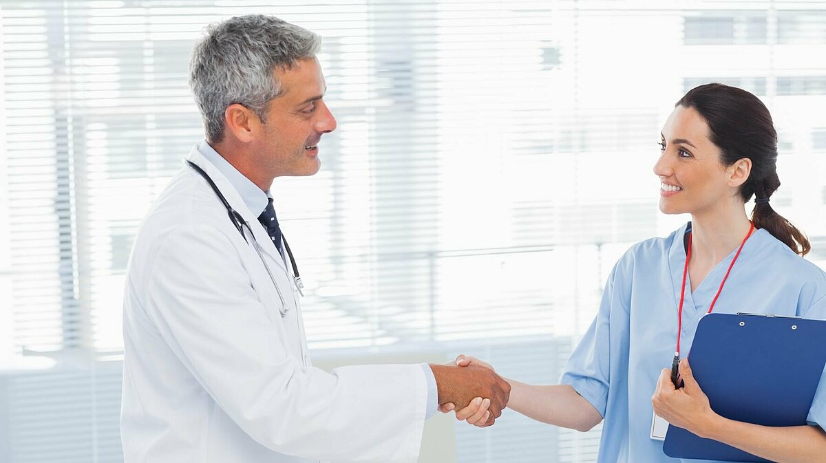 Arzt gibt mitarbeiterin die Hand und lächelt sie dabei freundlich an.