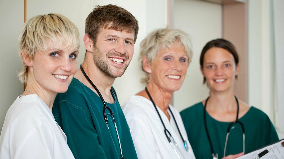Ärztin steht mit drei Praxismitarbeitern zusammen und lächelt in die Kamera.